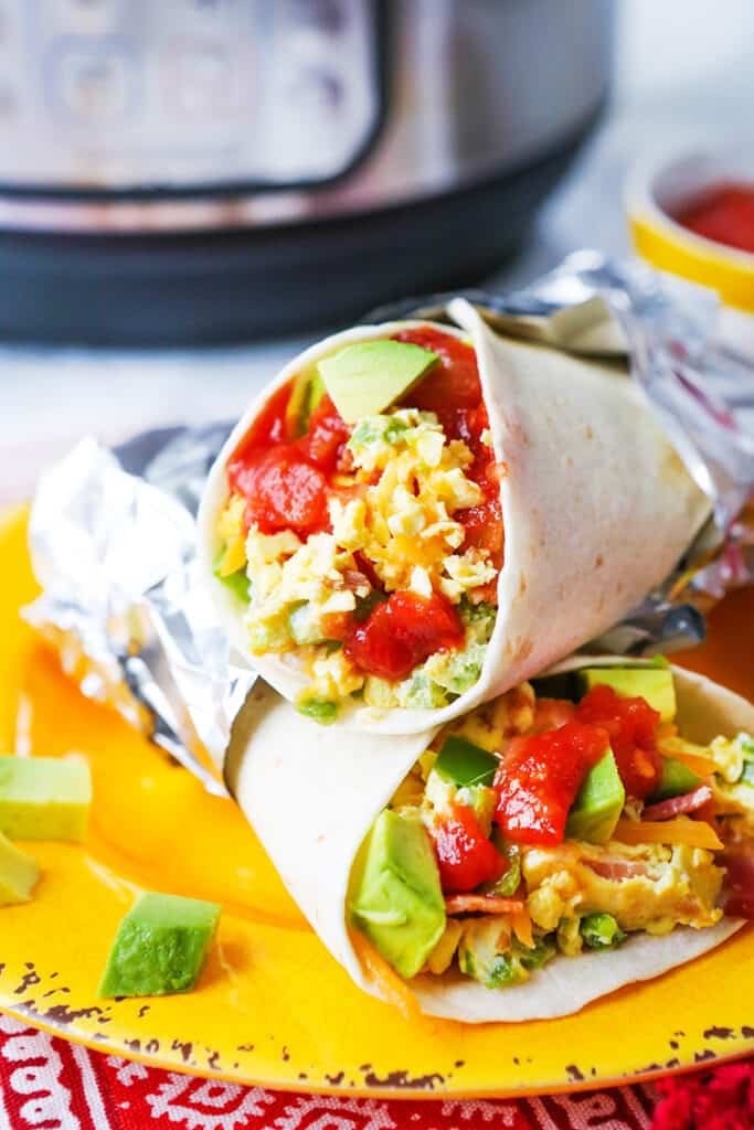 Two breakfast burritos stacked on a yellow plate.