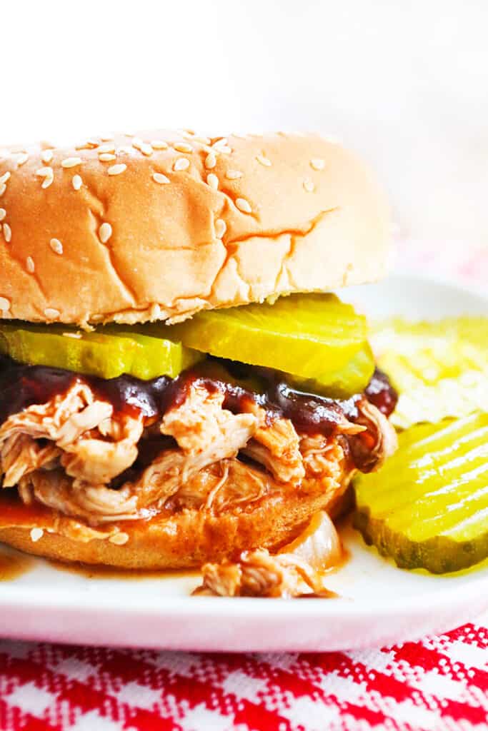 pulled pork on a sesame bun with pickles and bbq sauce sitting on a plate