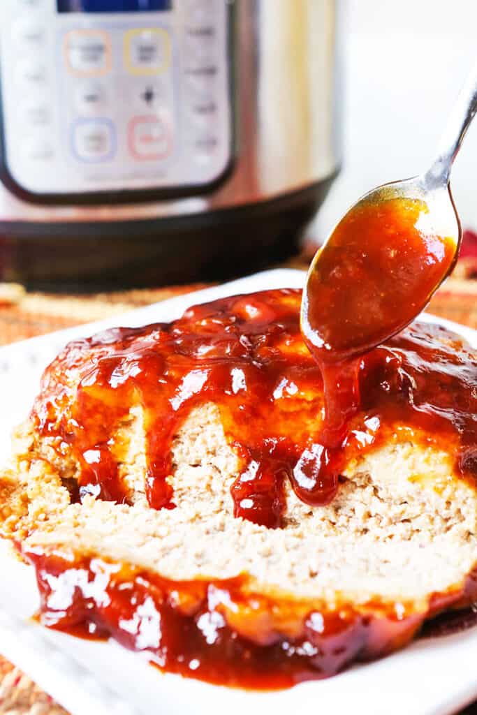 Spoon drizzling red sauce over meatloaf, sitting next to Instant Pot.