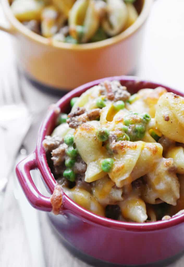 Two bowls full of pasta, peas and beef with forks nearby