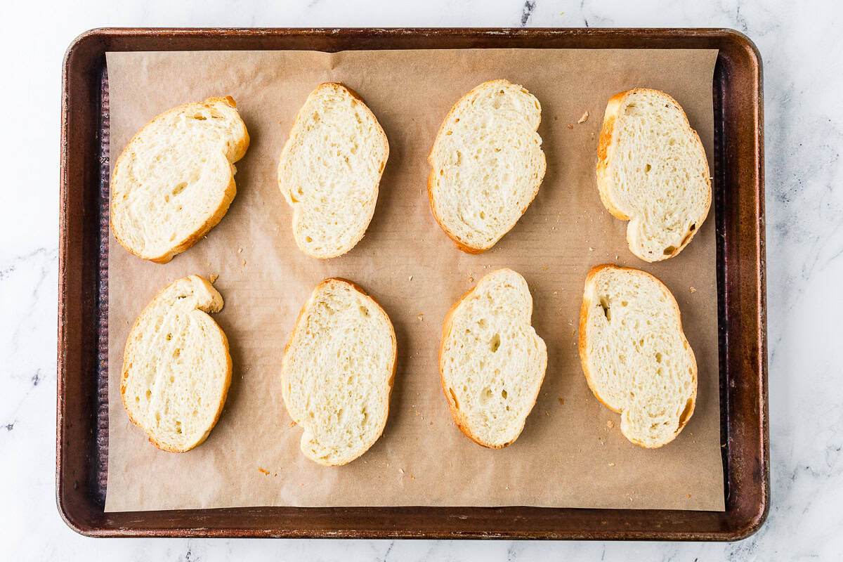 Eight baguette slices on a baking sheet.