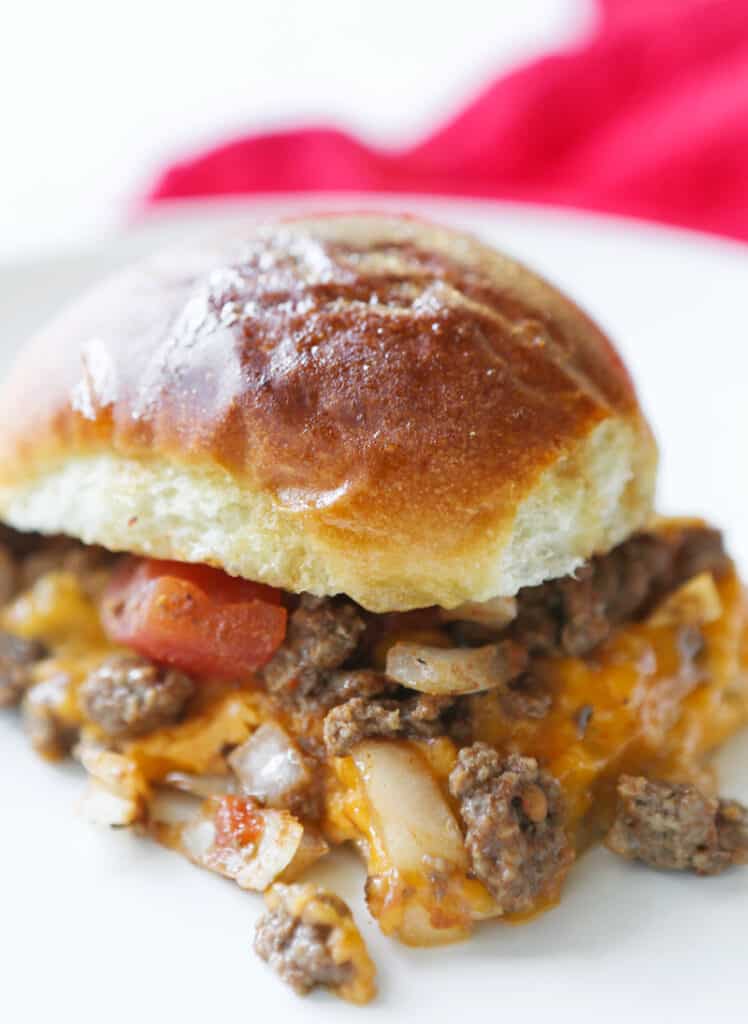 Single meaty sandwich sitting on a white plate with ground beef and cheese spilling out sides.