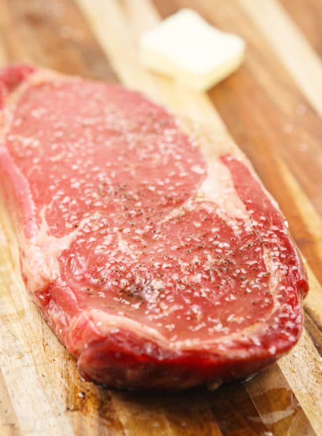 uncooked ribeye steak covered in salt and pepper on cutting board