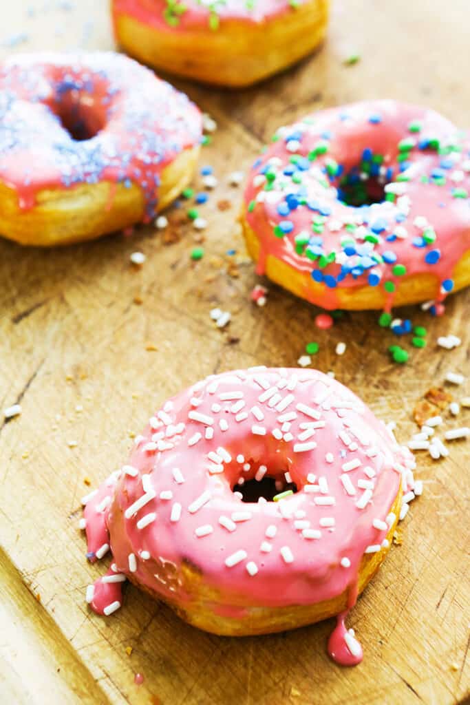 easy air fryer donuts with pink glaze and sprinkles sitting on top of a wooden cutting board.