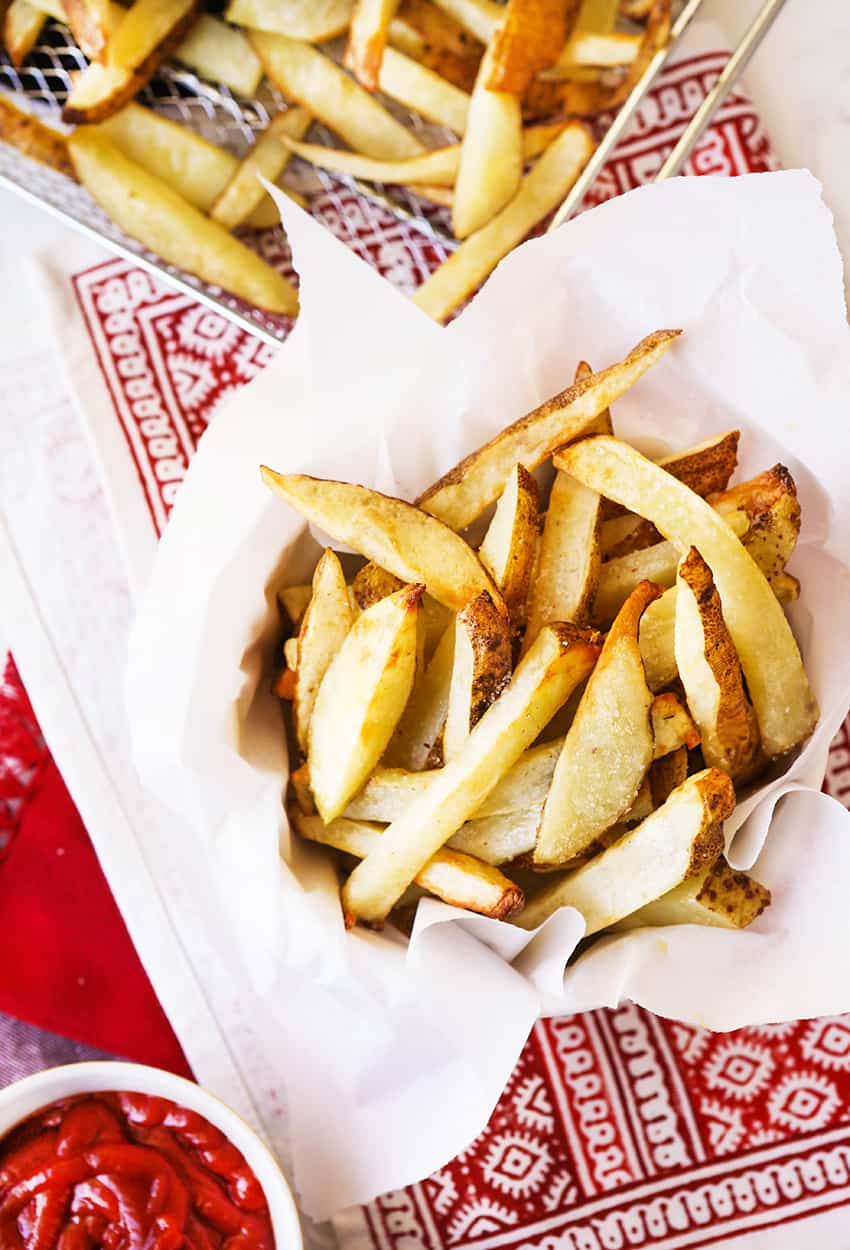 French fries in parchment paper next to air fryer tray and ketchup.