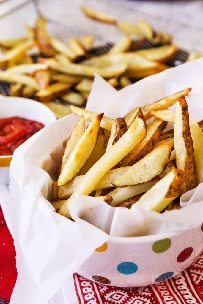 Fries in a serving bowl next to a small bowl of ketchup.
