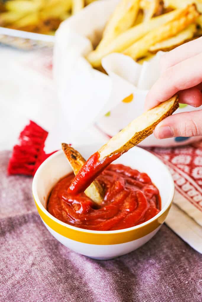 hand dipping a fry into a bowl of ketchup