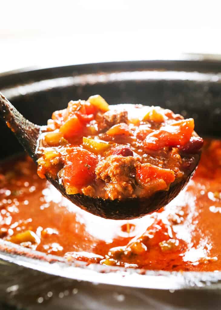 ladle filled with chili hovering over slow cooker