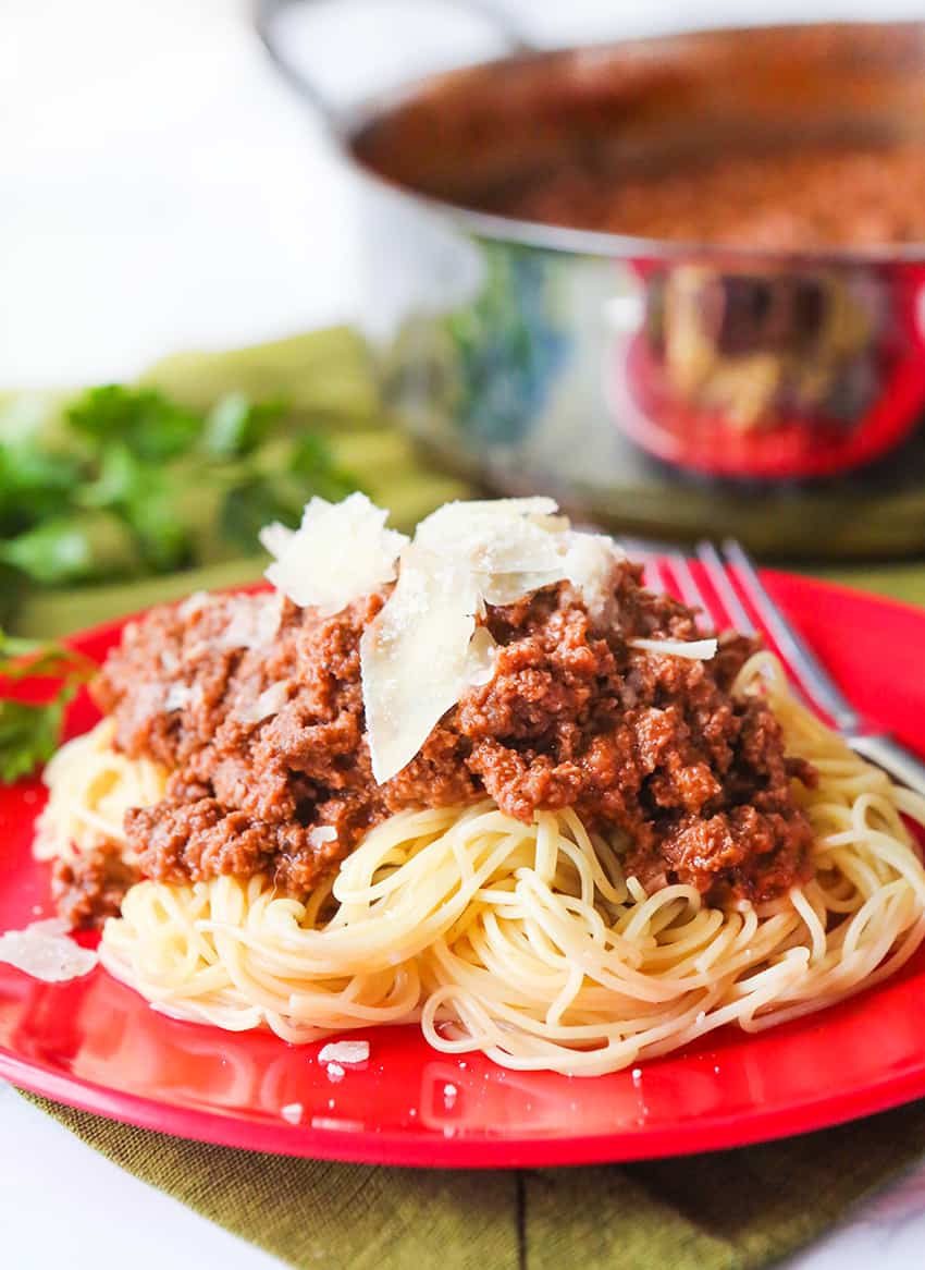 Cooked angel hair pasta with meaty pasta sauce and shaved parmesan on top.