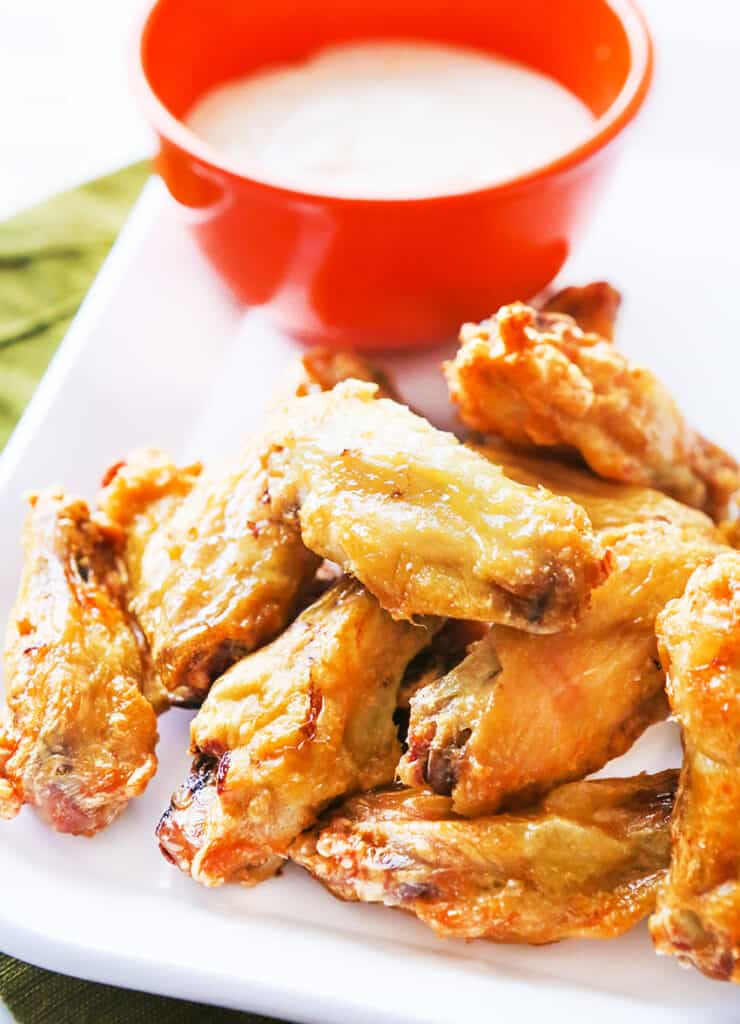 Chicken wings on a serving plate, next to a bowl filled with blue cheese dressing.