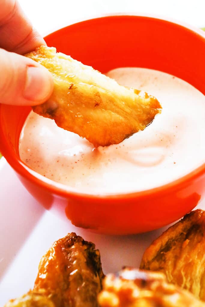 hand dipping a chicken wing into white dipping sauce