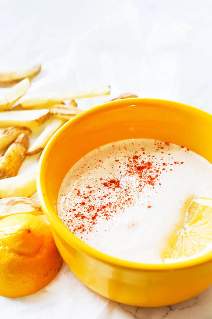 bowl of seasoned sour cream sprinkled with paprika and sitting next to fries