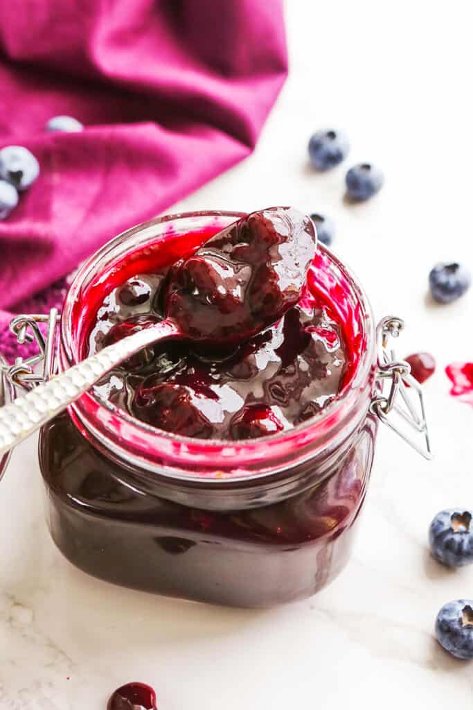 jar of blueberry sauce with spoon resting on jar and fresh blueberries surrounding it