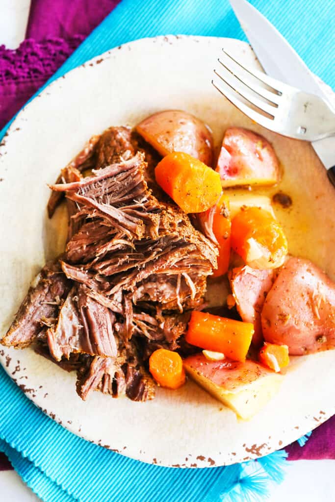 top view of plate of roast, carrots and potatoes with knife and fork resting on plate