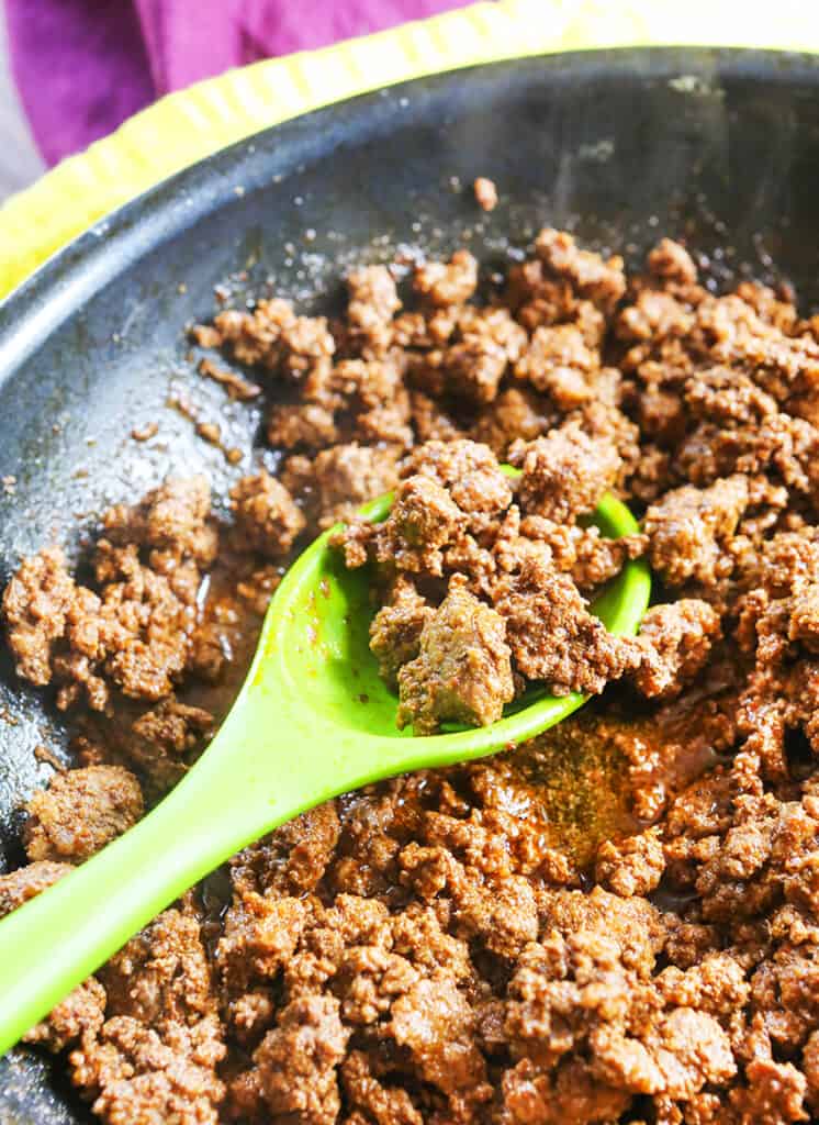 skillet of taco meat with green mixing spoon inside.