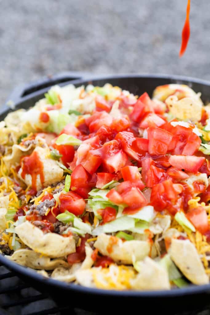 drip of hot sauce falling into skillet filled with nachos