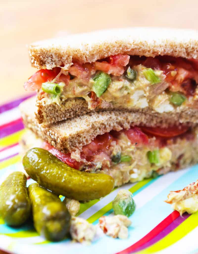 tuna salad sandwich cut in half and stacked on plate with pickles