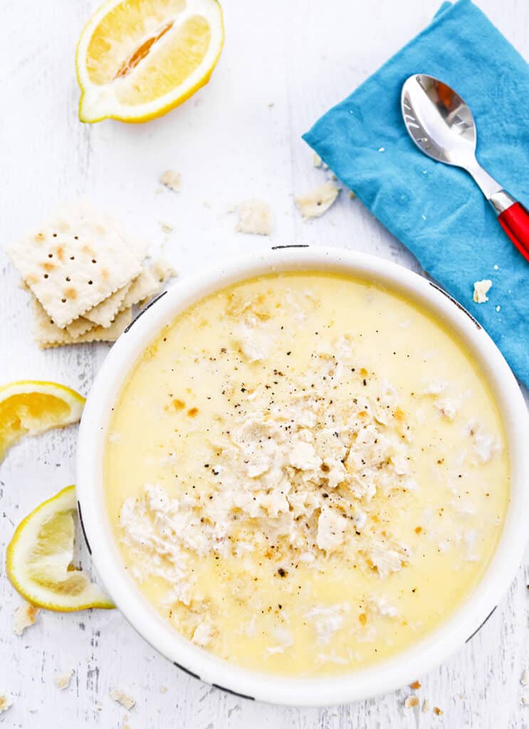 top view bowl of crab soup with saltines and lemons surrounding it