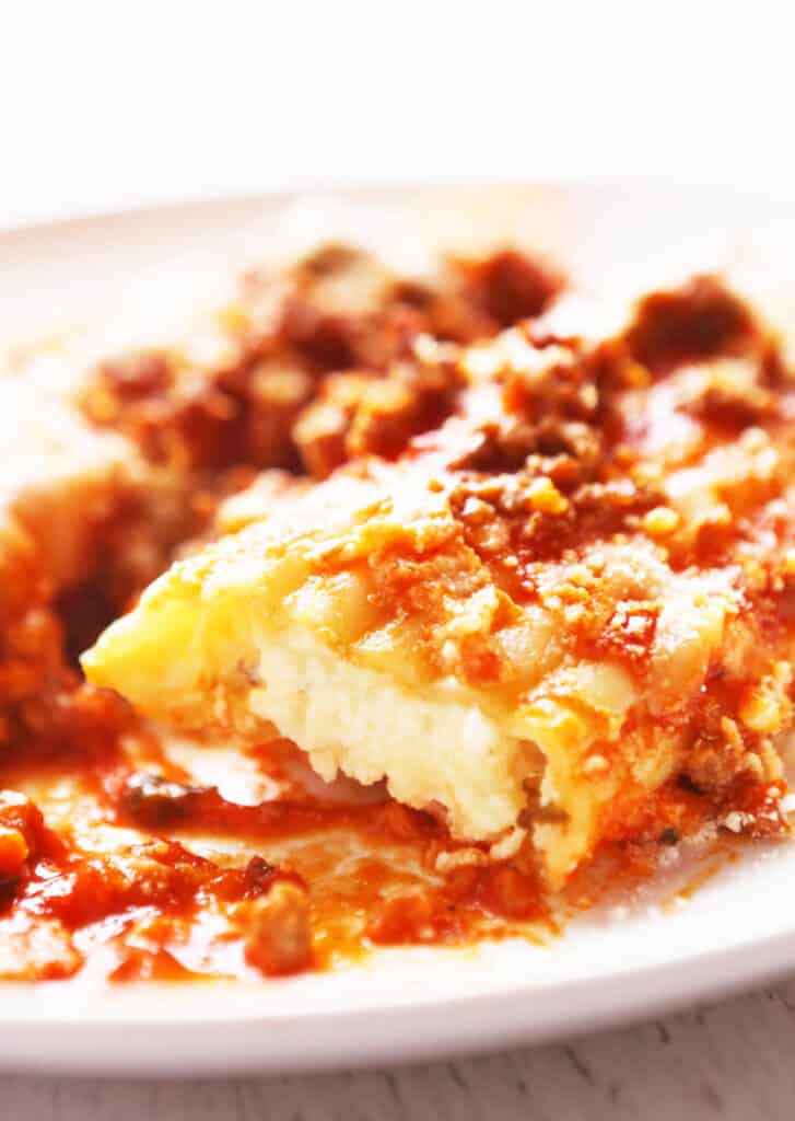 close up of a manicotti noodle oozing with cheese and meaty sauce mixture over top.