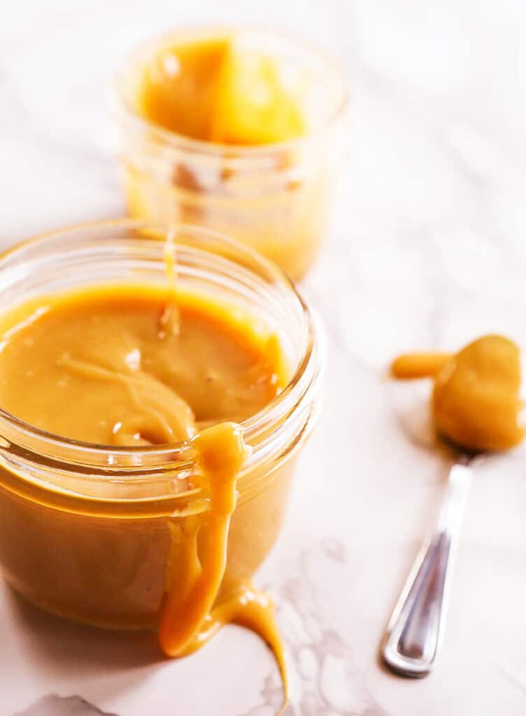 dulce de leche in mason jar, dripping down side with spoon nearby