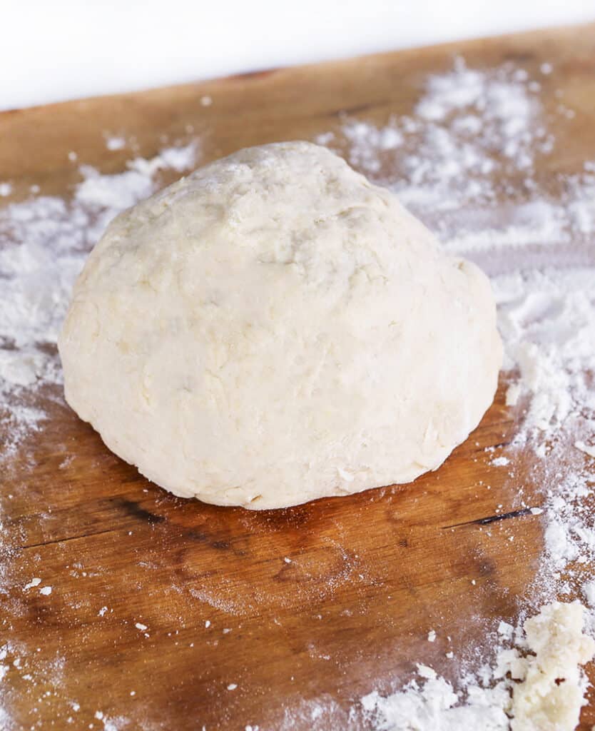 ball of pizza dough sitting on a cutting board with flour