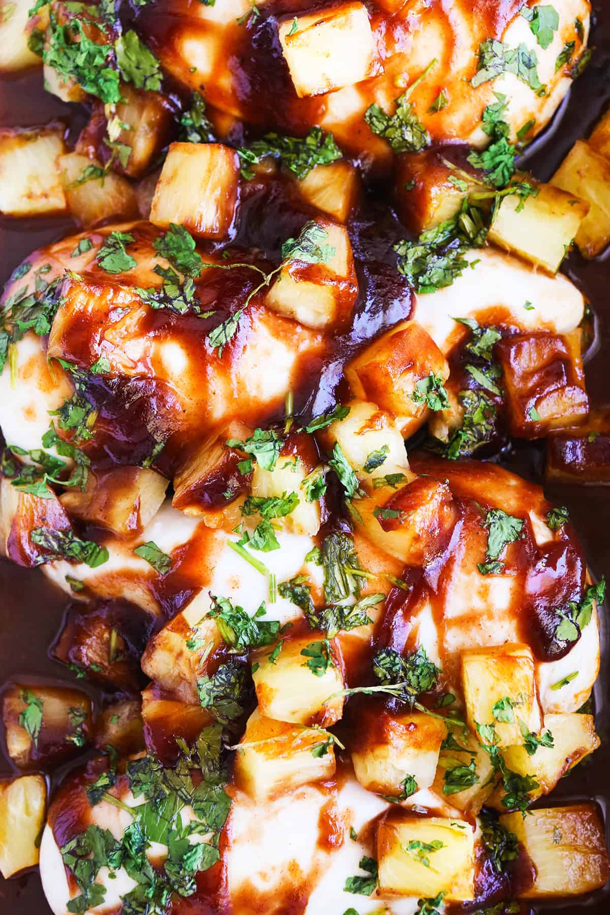 Top view of baked chicken in a pan, swimming in bbq sauce and pineapple chunks.
