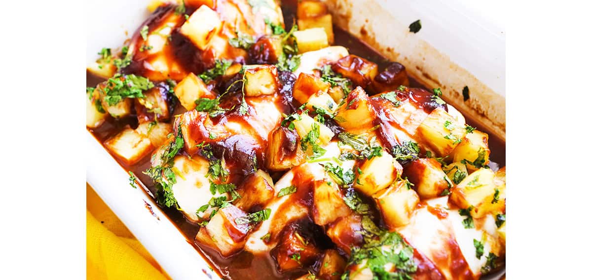 Chicken, barbecue sauce, pineapple chunks and parsley in a baking dish.