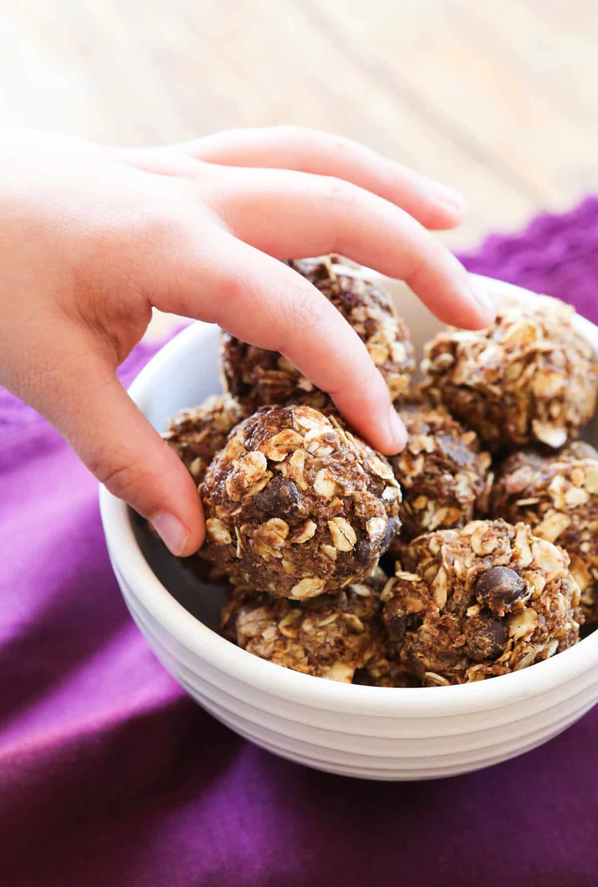 Small hand reaching into frame to grab a snack bite from a bowl.