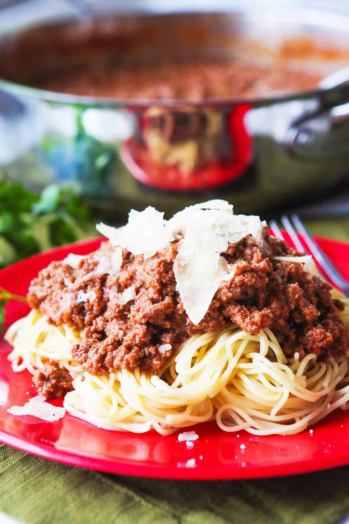 Spaghetti with meat sauce topped with cheese on a red plate.