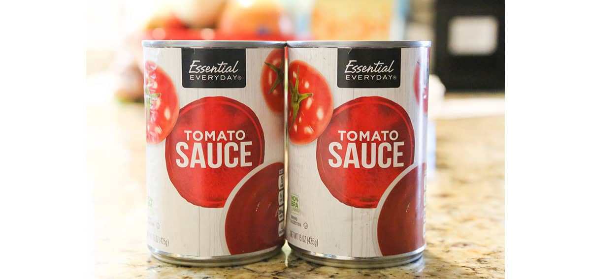 Two cans of tomato sauce on a kitchen countertop for spaghetti sauce.