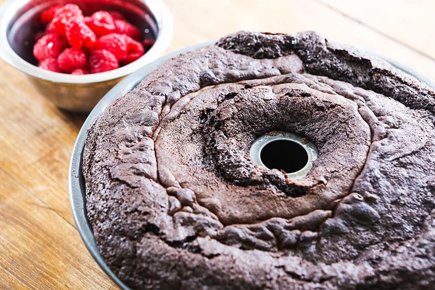 baked chocolate cake in bundt pan sitting next to a bowl of raspberries