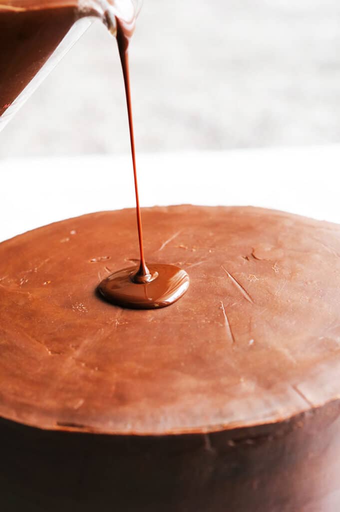 chocolate ganache being poured over perfectly frosted layer cake