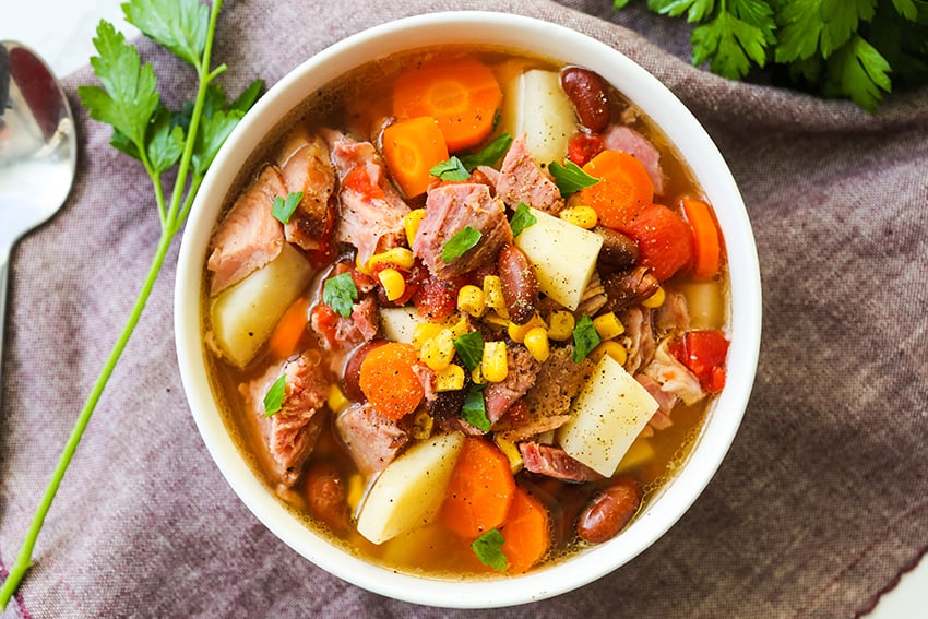 bowl of ham and veggie soup with parsley and a spoon sitting next to it