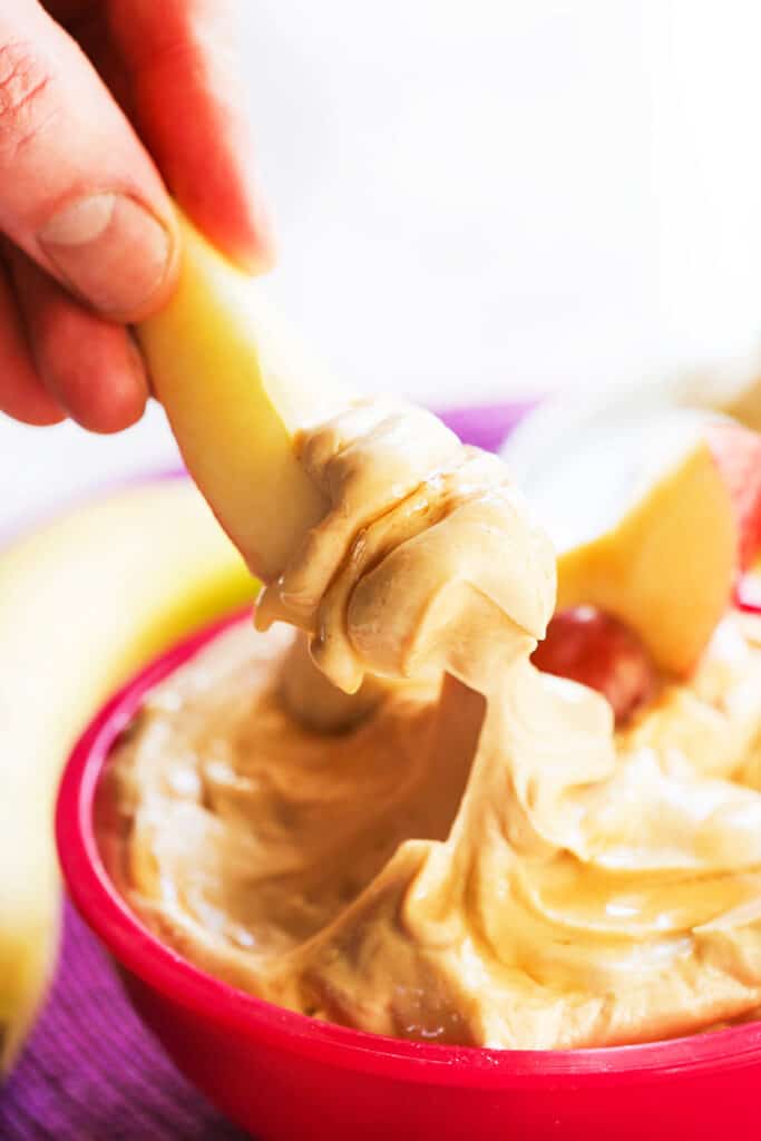 hand dipping an apple slice into a creamy dip
