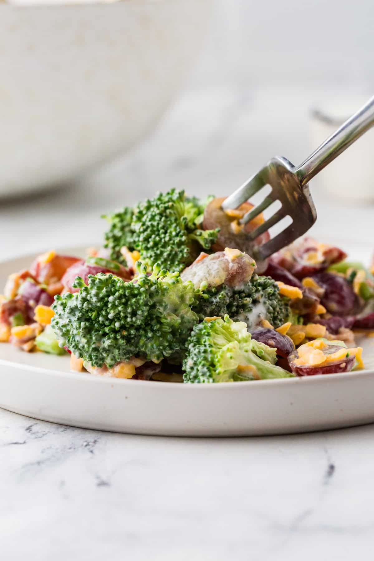 A fork grabbing a bite from a plate filled with broccoli salad.