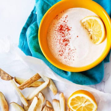 Creamy sour cream dip with lemon slice and paprika in yellow bowl.