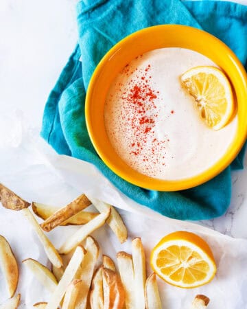 Creamy sour cream dip with lemon slice and paprika in yellow bowl.