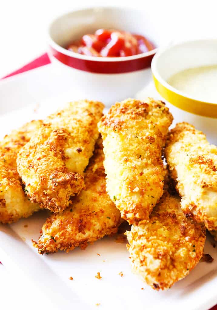 chicken tenders stacked on a serving plate next to a dipping sauce