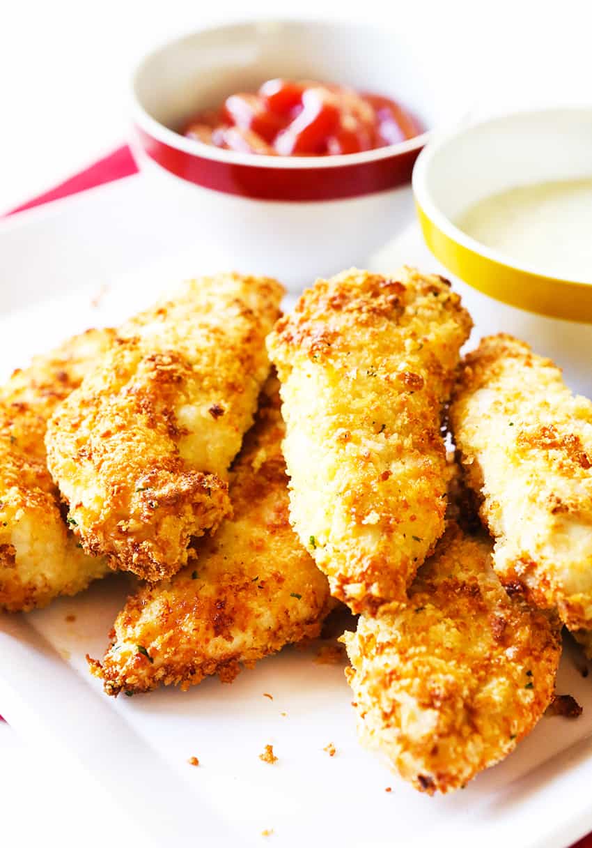 Air fryer chicken tenders on a plate with a side of ketchup in a small bowl. 