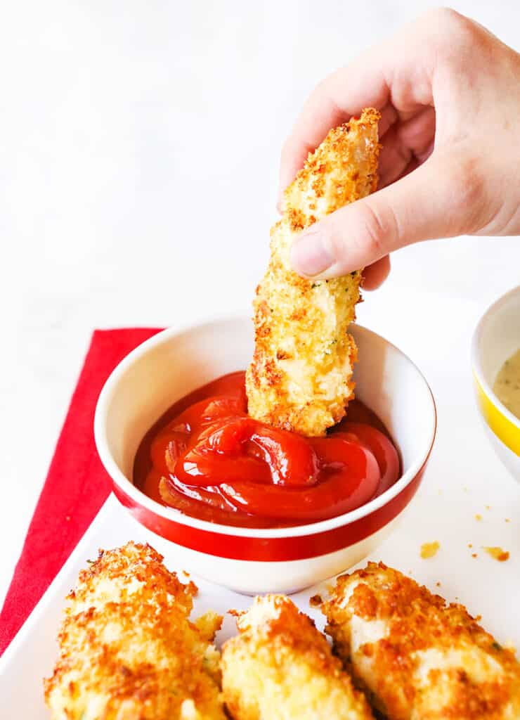 hand dunking a chicken tender into ketchup