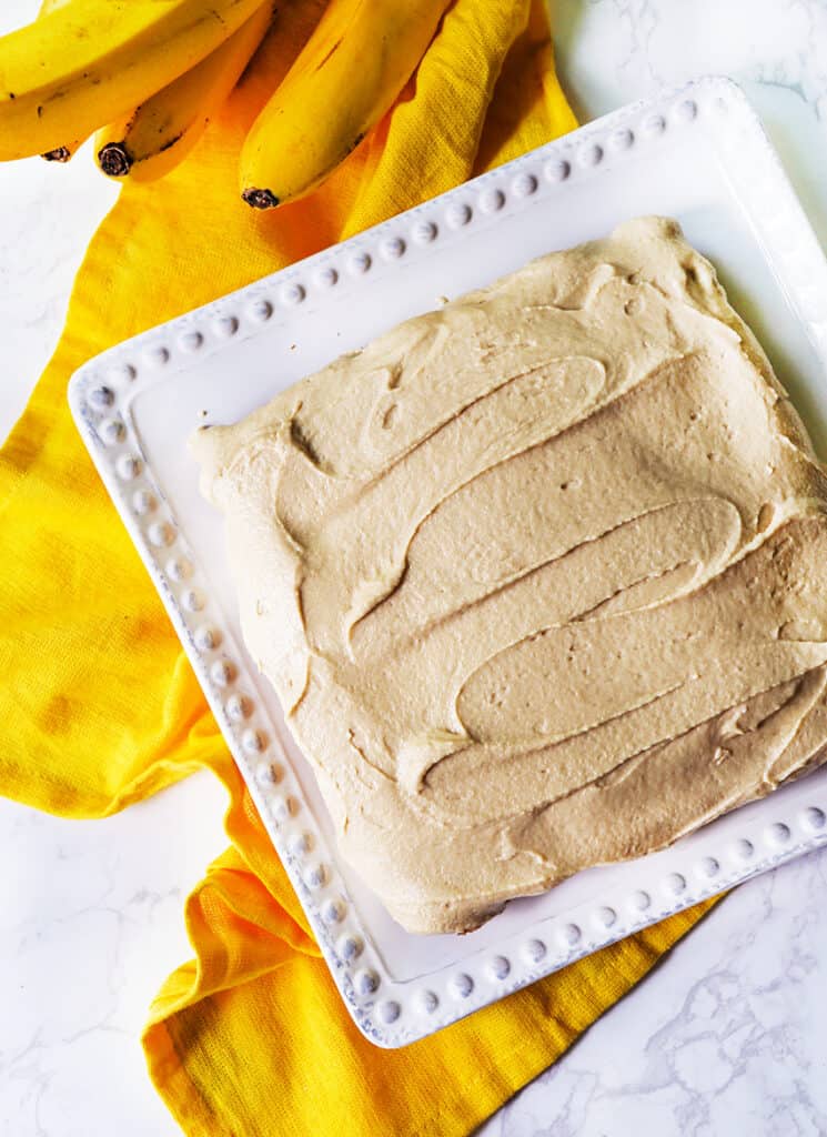 top view of cake covered with frosting and sitting next to a bunch of bananas