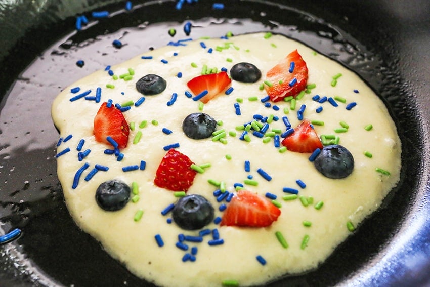 pancake in a skillet with berries and sprinkles
