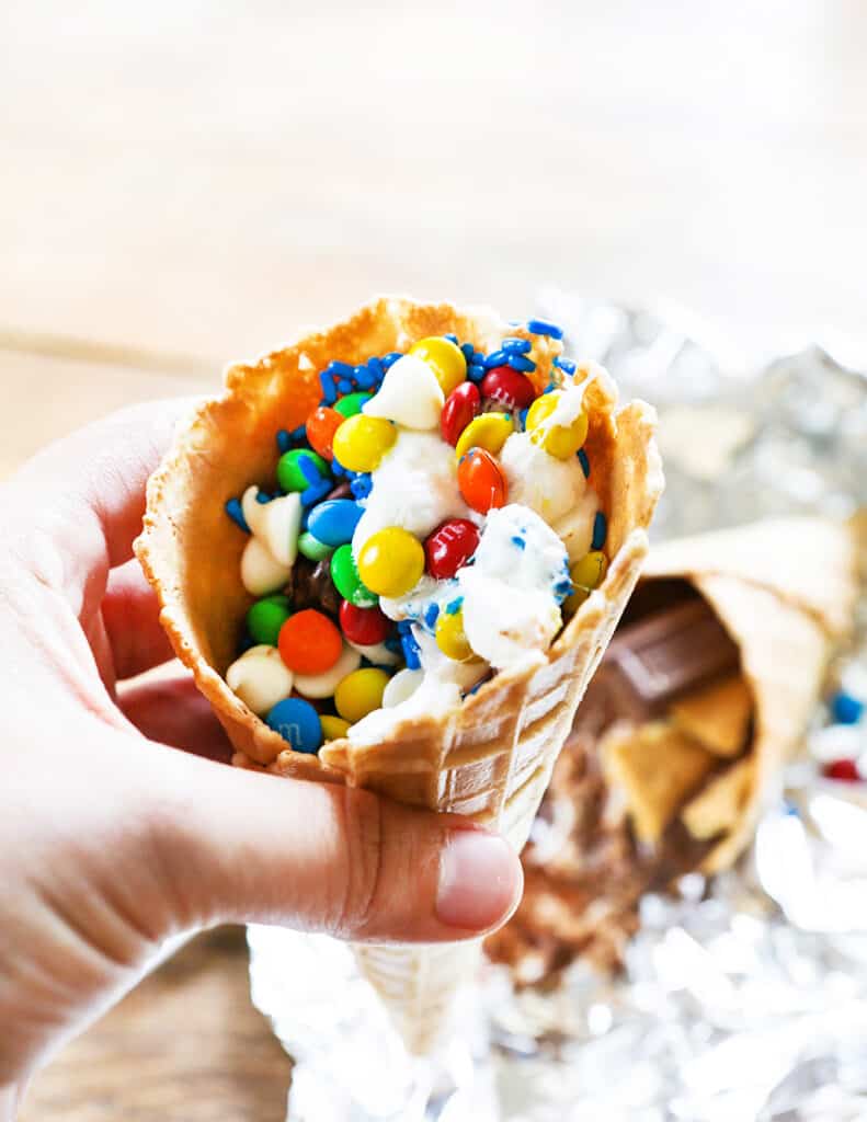hand holding waffle cone stuffed with candy and sugary ingredients