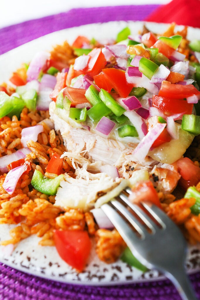 fork pulling piece of fiesta lime chicken off a breast topped with chunky colorful salsa