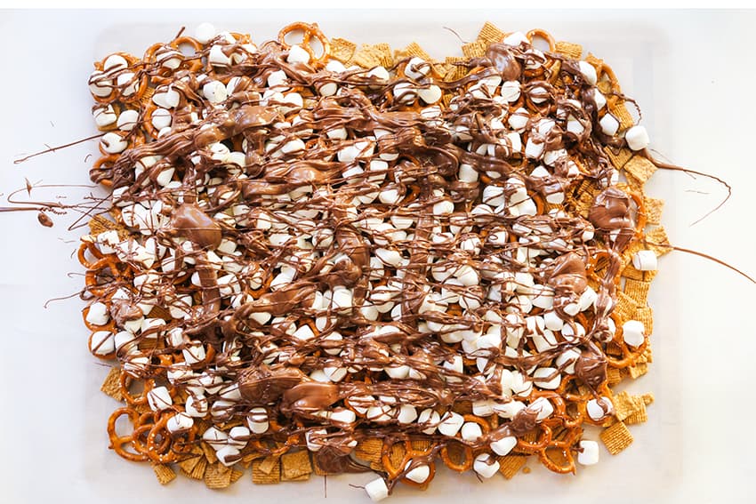 Layers of s'mores snack mix ingredients on parchment paper