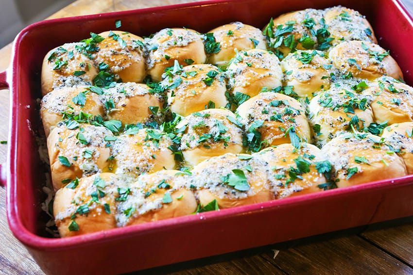 rolls with seasoning on top of pizza sliders in a baking dish