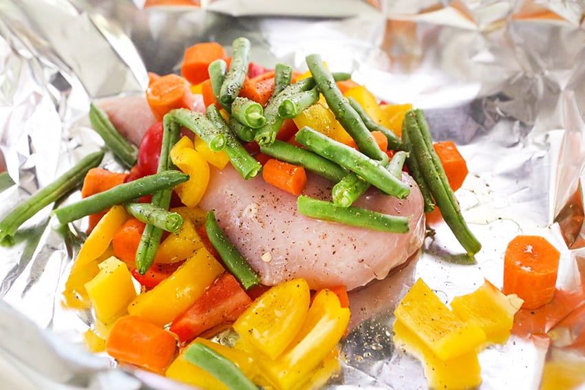 chicken breast on foil with veggies surrounding it