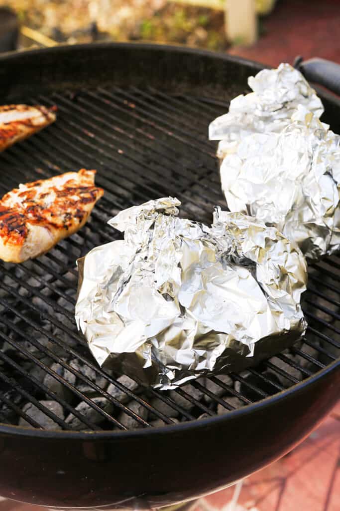 foil pouches on grill next to grilled chicken breasts