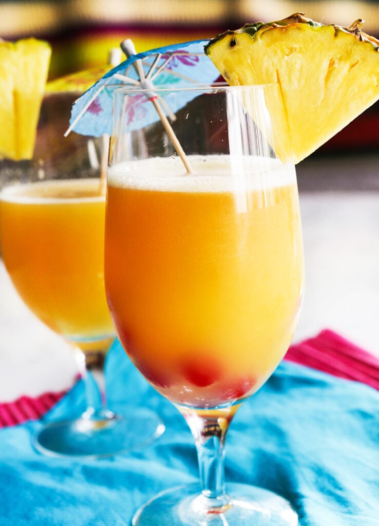 side view of two tropical drinks with pineapple wedges on rims