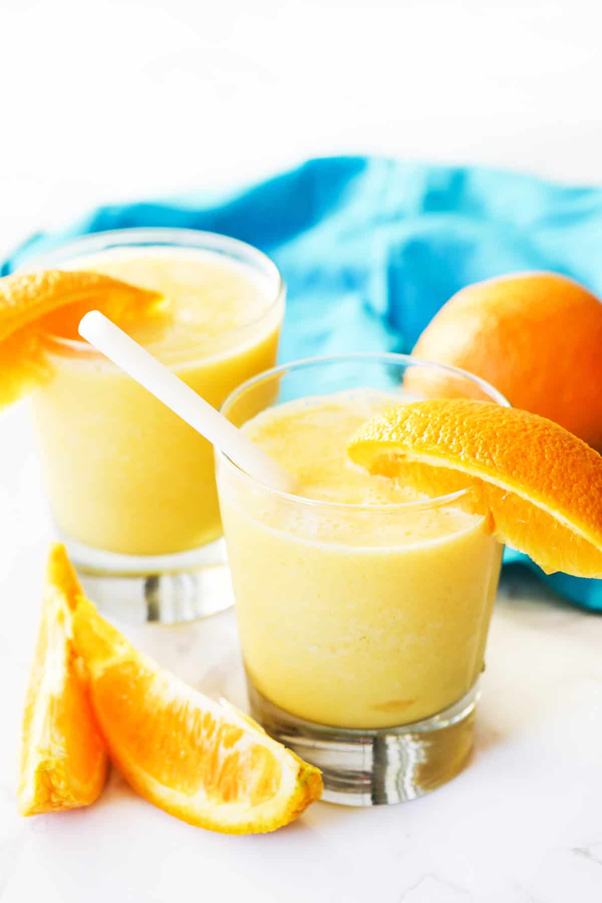Two glasses with an orange julius mixture inside and glasses are rimmed with orange slices.